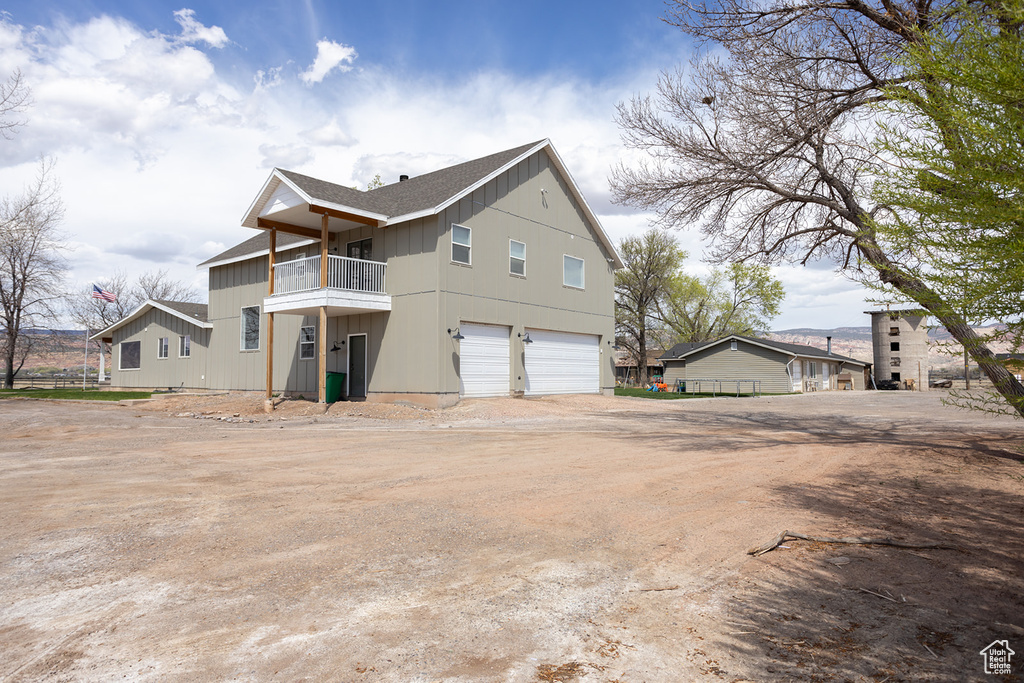 View of property exterior featuring board and batten siding, a balcony, dirt driveway, and a garage
