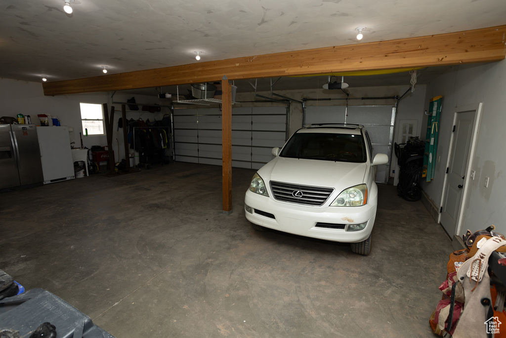 Garage with a garage door opener, stainless steel refrigerator with ice dispenser, and freestanding refrigerator