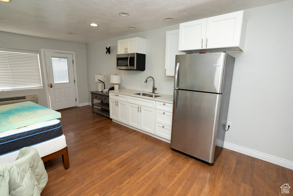 Kitchen featuring dark wood-style floors, a sink, stainless steel appliances, white cabinetry, and baseboards