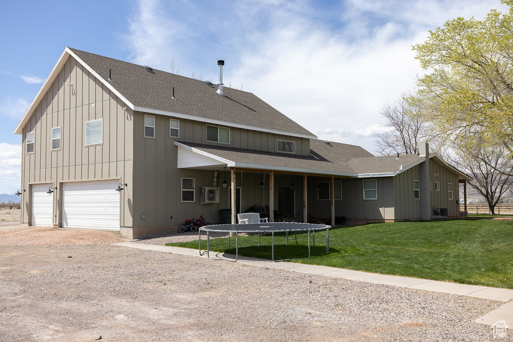 View of front of property featuring a front yard, a trampoline, dirt driveway, board and batten siding, and an attached garage