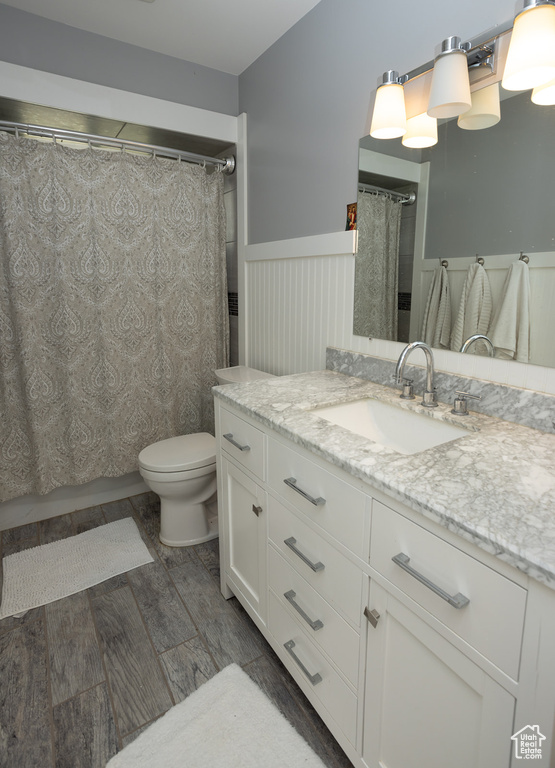 Bathroom with vanity, curtained shower, toilet, a wainscoted wall, and wood finished floors
