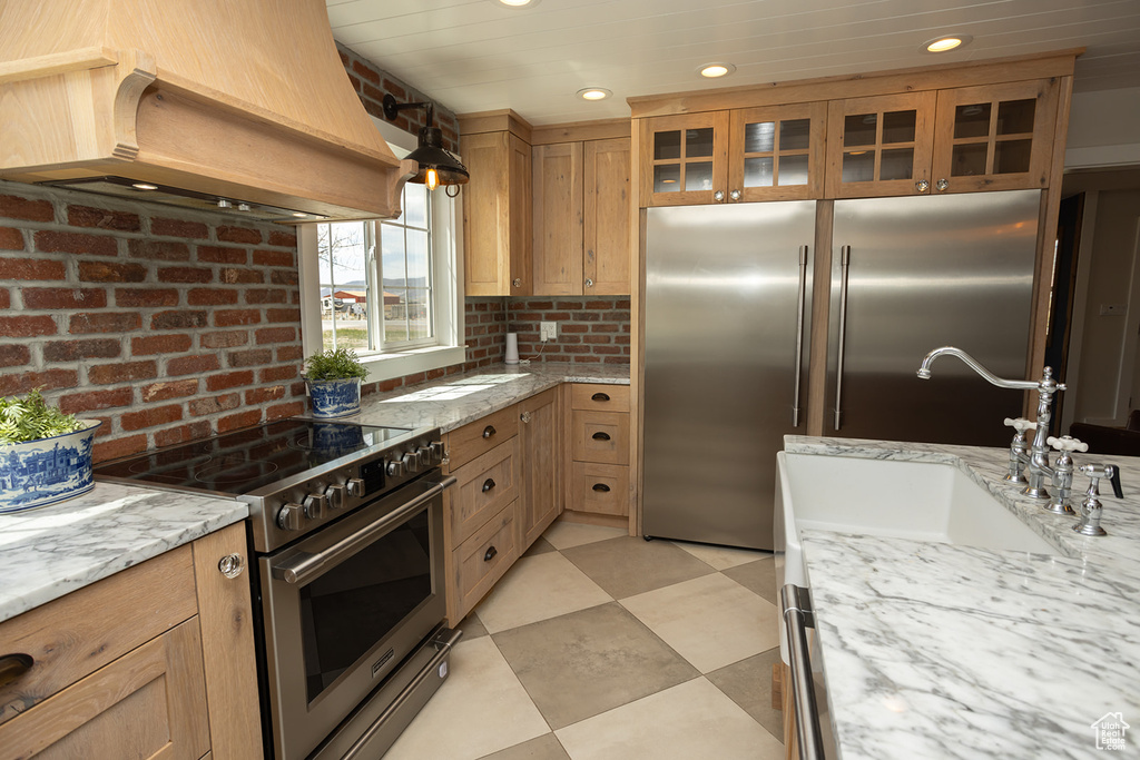 Kitchen featuring recessed lighting, light floors, glass insert cabinets, custom range hood, and high quality appliances