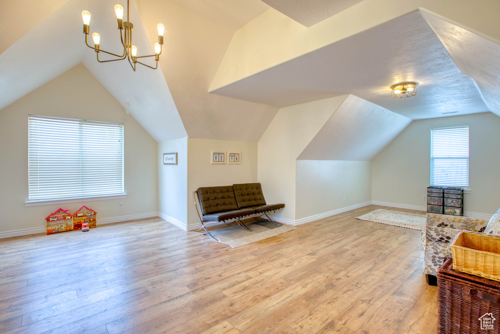 Additional living space featuring a chandelier, baseboards, light wood-style floors, and lofted ceiling