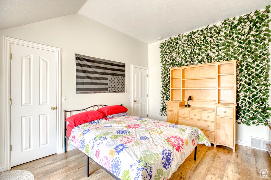Bedroom with lofted ceiling, visible vents, light wood-style flooring, and baseboards