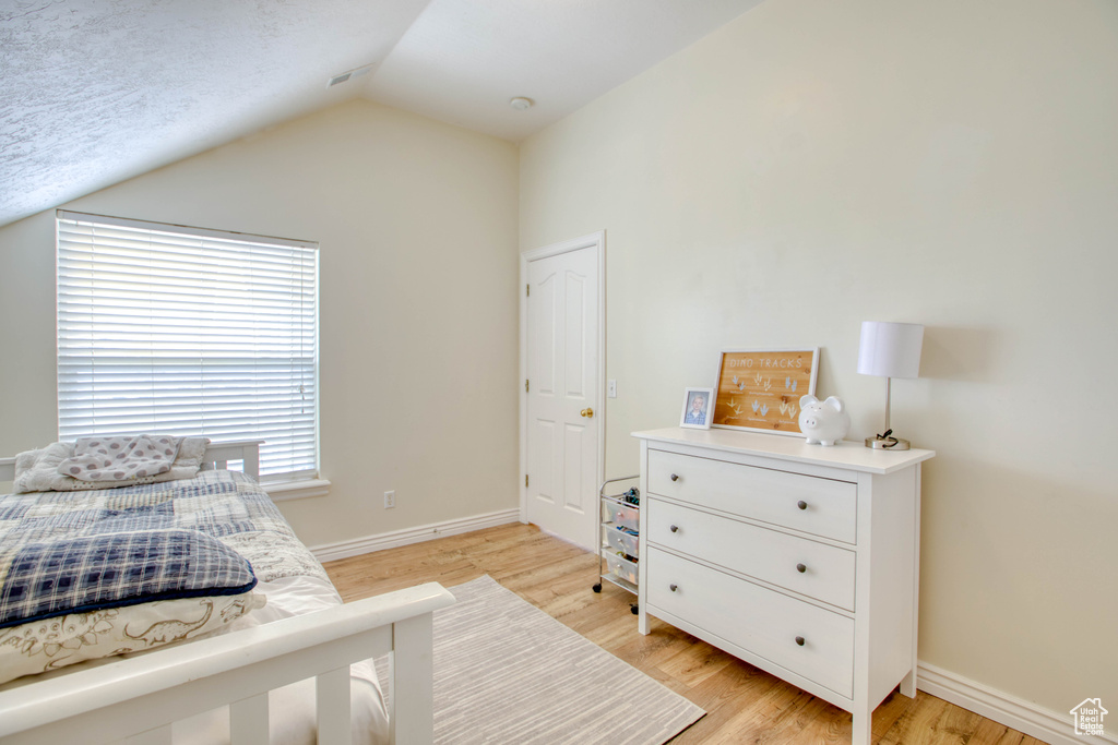 Bedroom featuring baseboards, light wood-style flooring, and vaulted ceiling