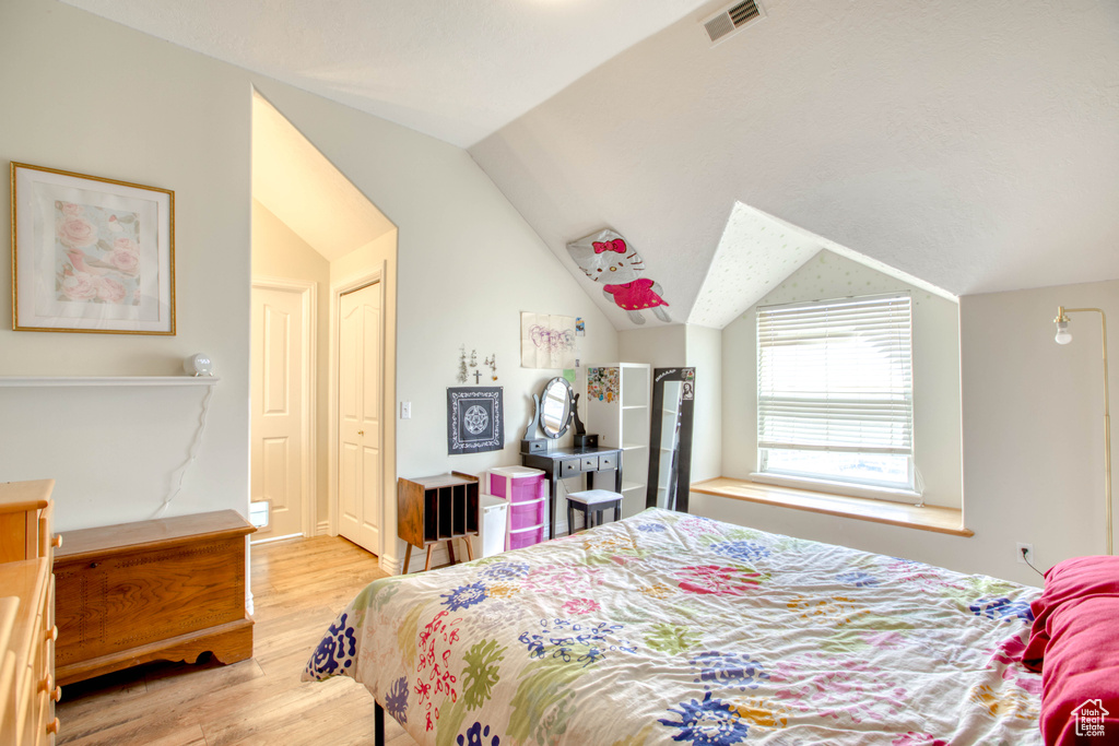 Bedroom with visible vents, lofted ceiling, and light wood-style floors
