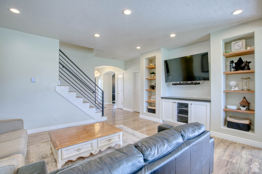 Living room featuring baseboards, arched walkways, light wood-type flooring, recessed lighting, and built in features