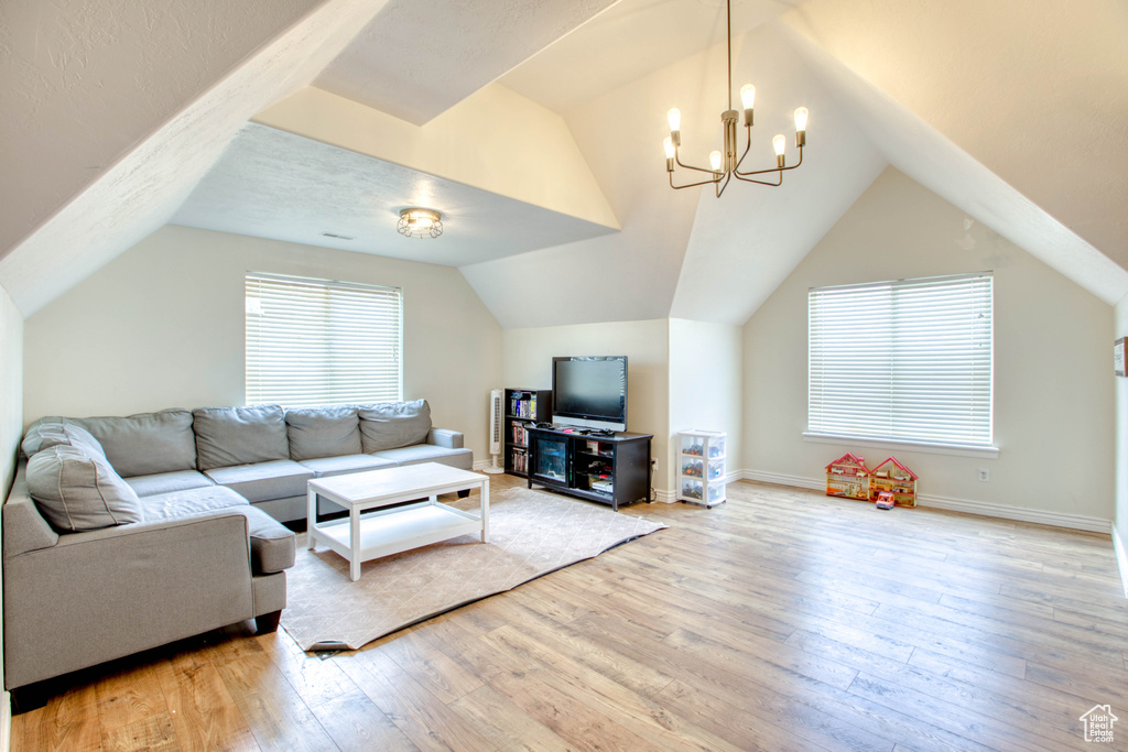 Living room featuring baseboards, a notable chandelier, light wood finished floors, and vaulted ceiling