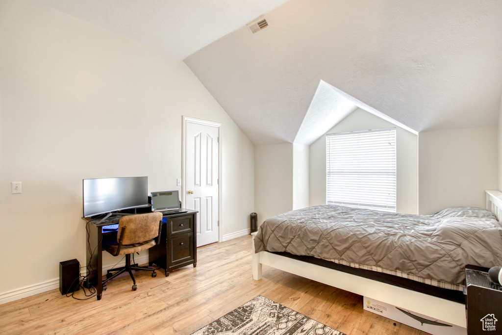 Bedroom featuring lofted ceiling, visible vents, light wood finished floors, and baseboards