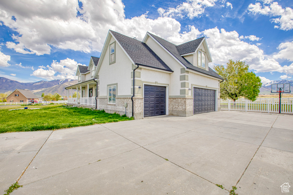 View of property exterior with fence, concrete driveway, a mountain view, stucco siding, and a yard
