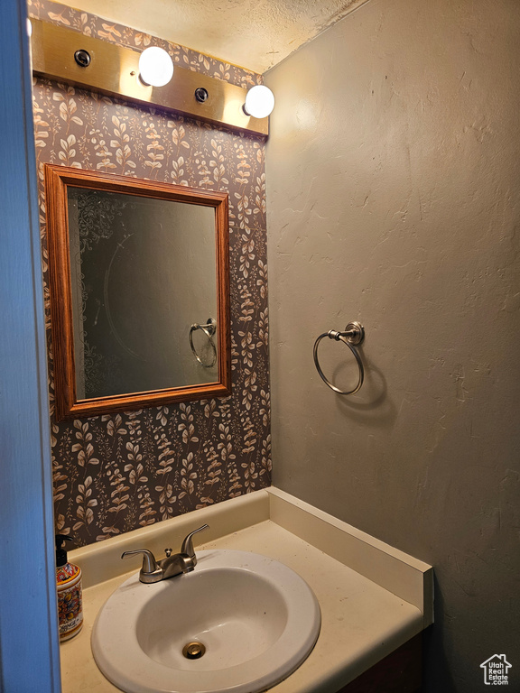 Bathroom with a textured ceiling, vanity, and wallpapered walls