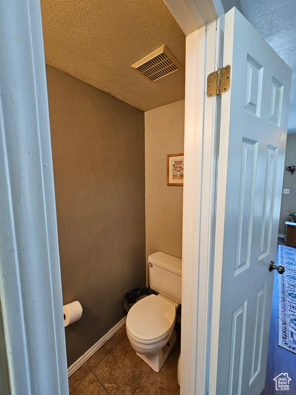 Bathroom with toilet, tile patterned floors, and a textured ceiling