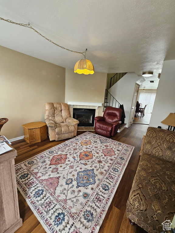 Living room with wood finished floors, a tile fireplace, a textured ceiling, and stairs