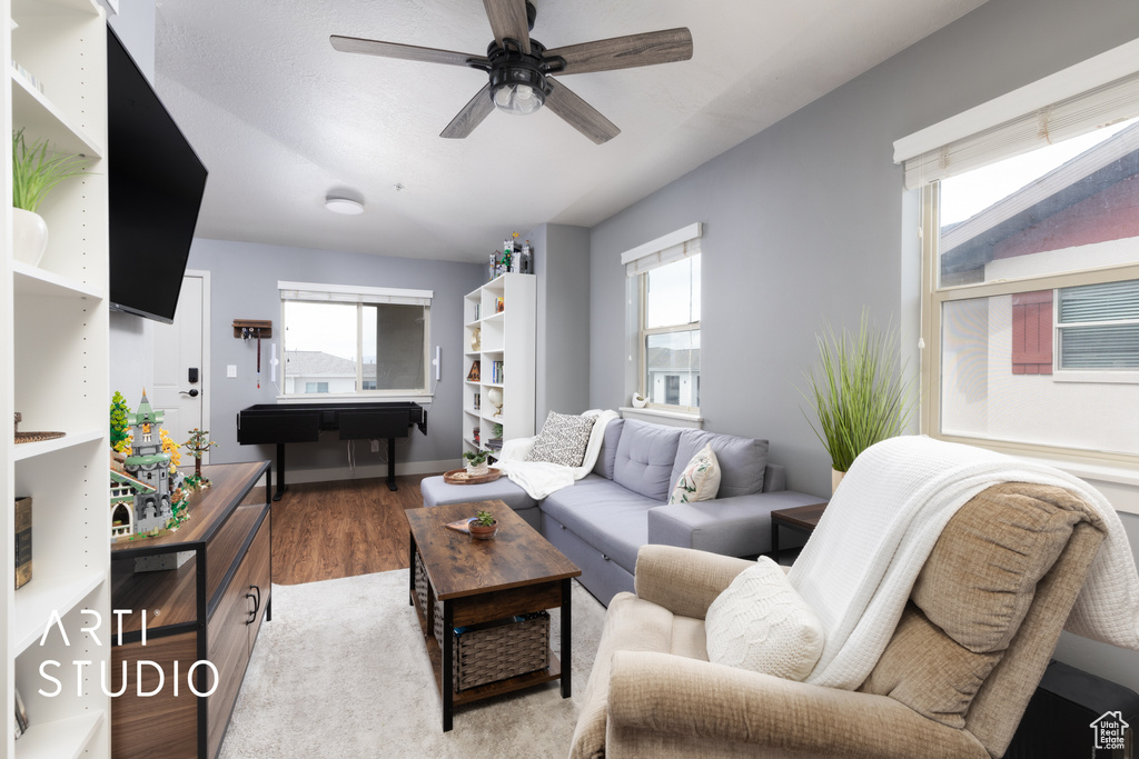 Living area featuring a ceiling fan, baseboards, wood finished floors, and a healthy amount of sunlight