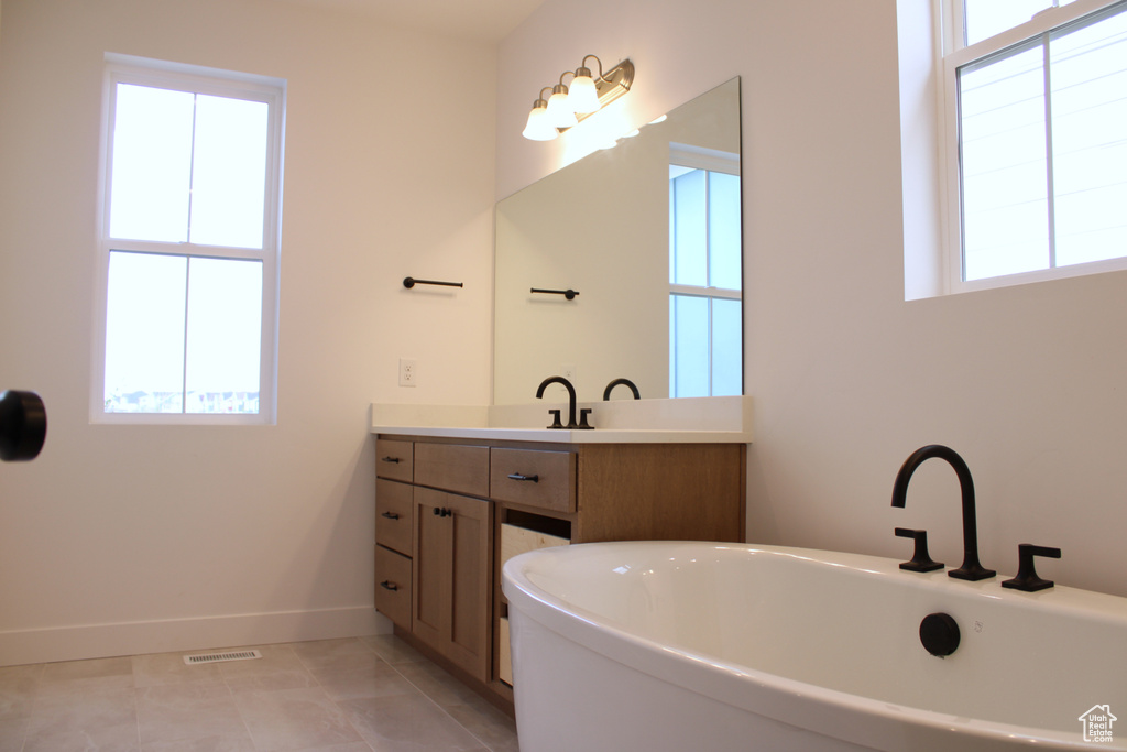 Bathroom with baseboards, visible vents, a freestanding bath, and vanity