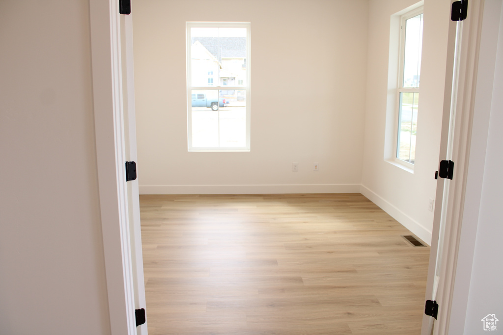 Empty room with baseboards, light wood-type flooring, visible vents, and a wealth of natural light