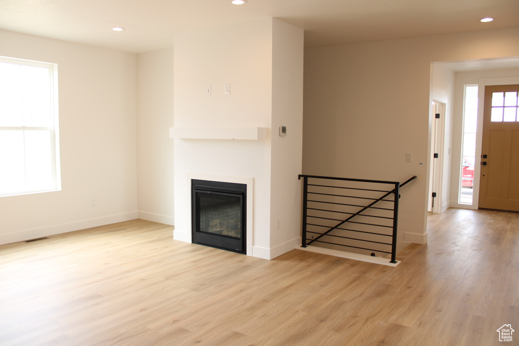 Unfurnished living room featuring light wood-style flooring, visible vents, baseboards, a glass covered fireplace, and recessed lighting