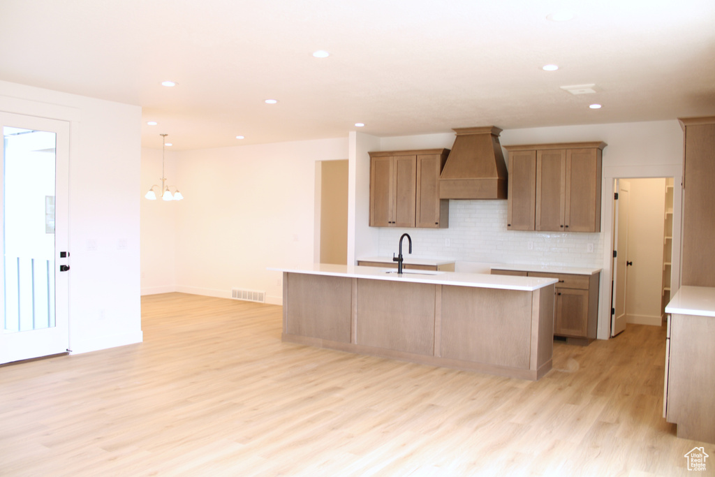 Kitchen with custom exhaust hood, decorative backsplash, light wood finished floors, a sink, and visible vents
