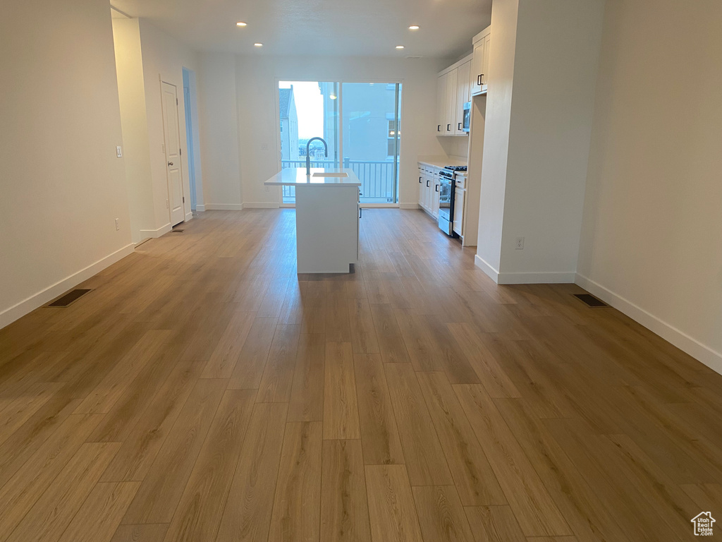 Kitchen featuring light wood finished floors, a center island with sink, visible vents, white cabinetry, and light countertops