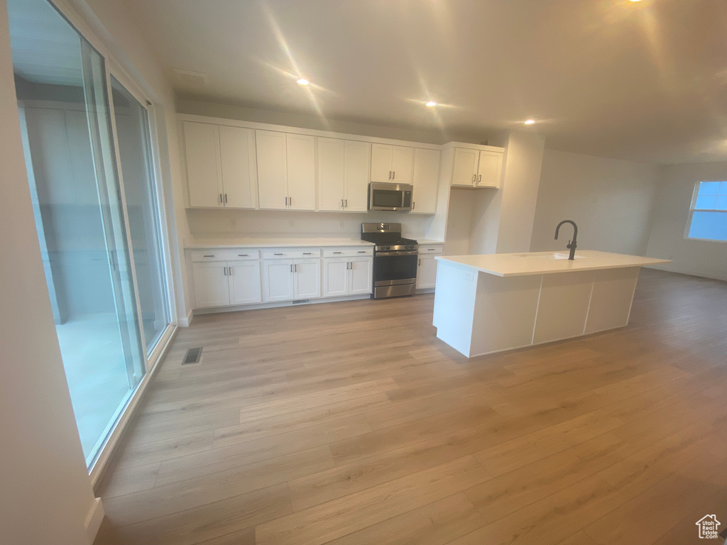 Kitchen with white cabinets, appliances with stainless steel finishes, visible vents, light countertops, and light wood-type flooring