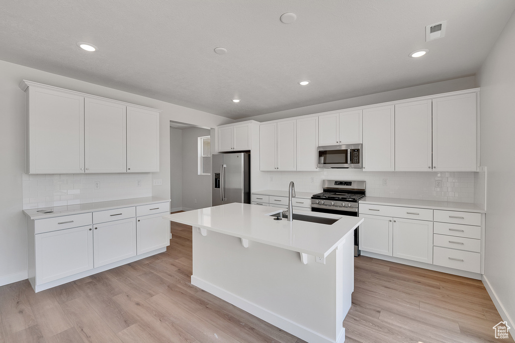 Kitchen with stainless steel appliances, a sink, light wood finished floors, decorative backsplash, and white cabinets