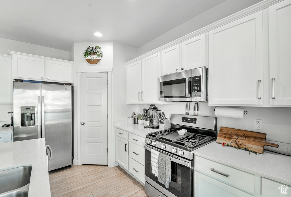 Kitchen with appliances with stainless steel finishes, light stone counters, white cabinets, light wood-style floors, and recessed lighting