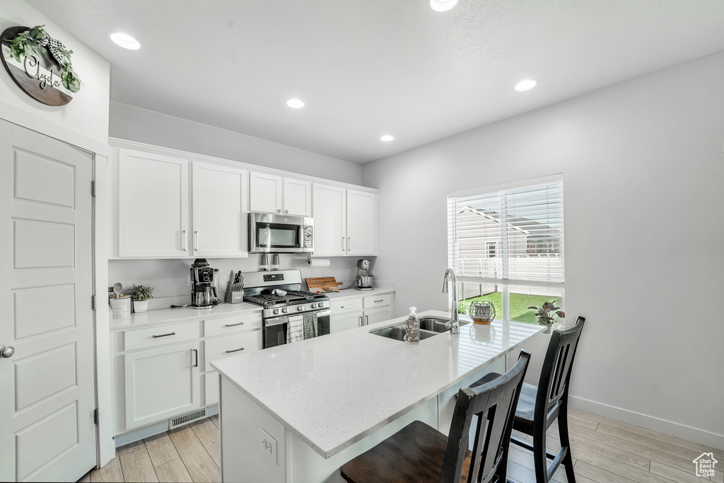 Kitchen featuring a kitchen island with sink, light wood-style floors, white cabinetry, a sink, and stainless steel appliances