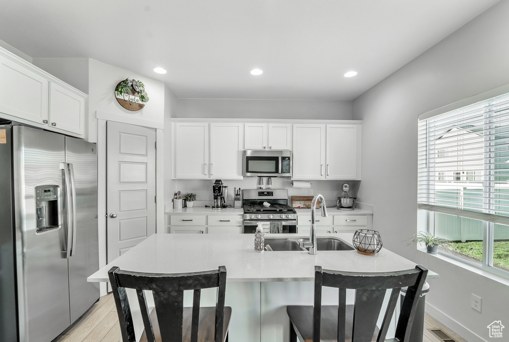 Kitchen featuring a sink, light countertops, white cabinets, stainless steel appliances, and light wood-style flooring