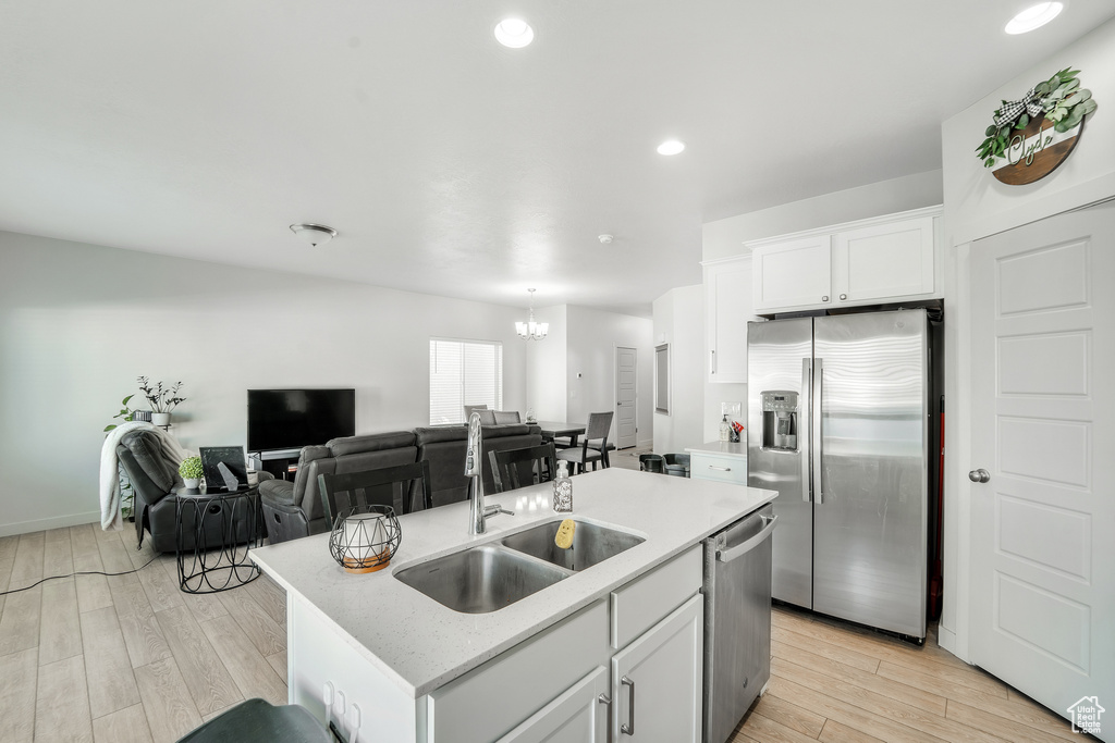 Kitchen with an inviting chandelier, a sink, stainless steel appliances, white cabinetry, and light wood-type flooring