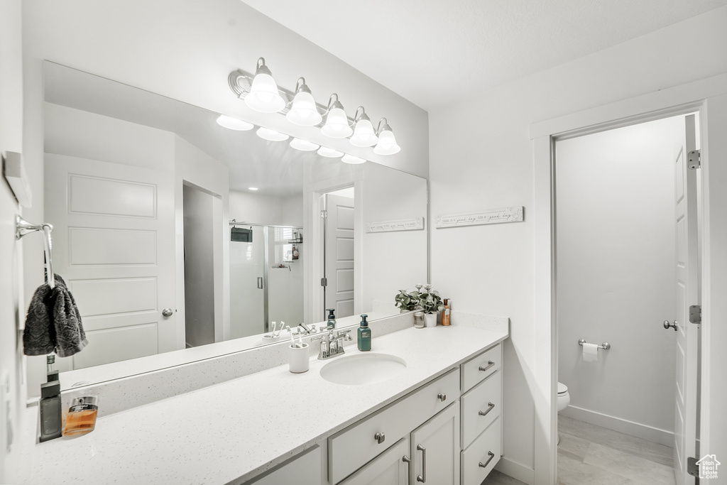 Bathroom featuring vanity, baseboards, a shower stall, and toilet