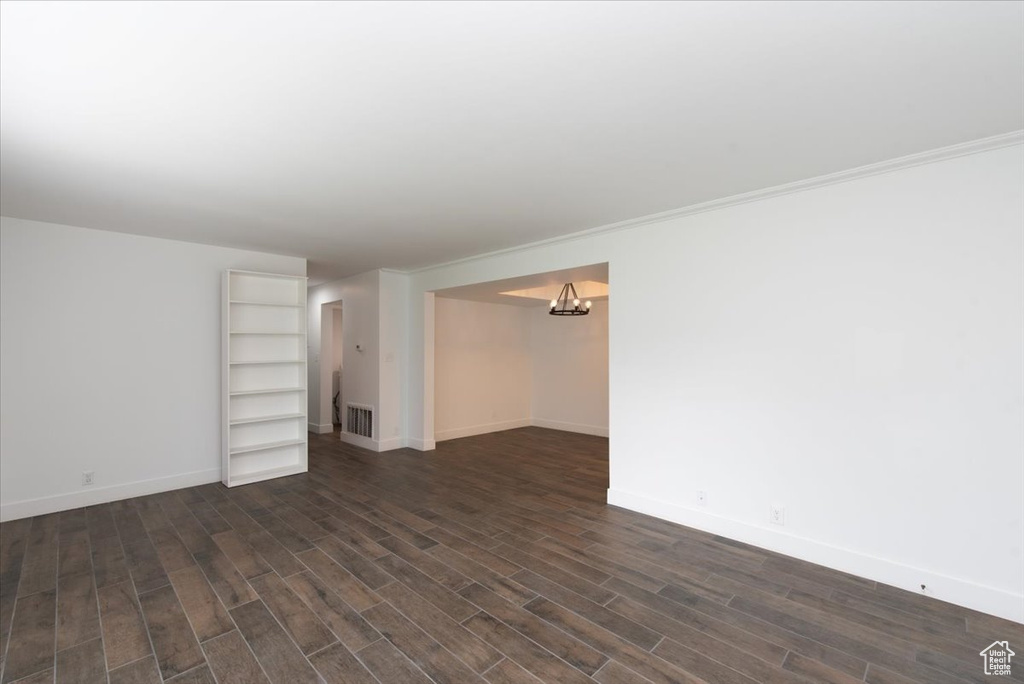 Unfurnished living room featuring an inviting chandelier, visible vents, dark wood finished floors, and baseboards