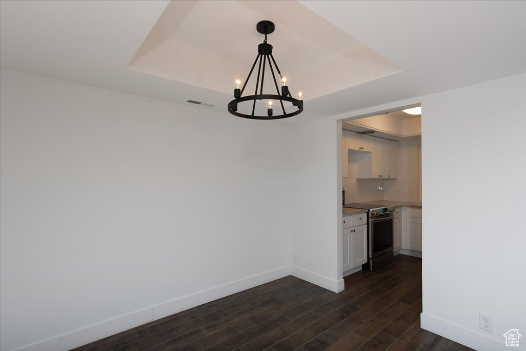 Unfurnished dining area with baseboards, a notable chandelier, dark wood-type flooring, and a tray ceiling