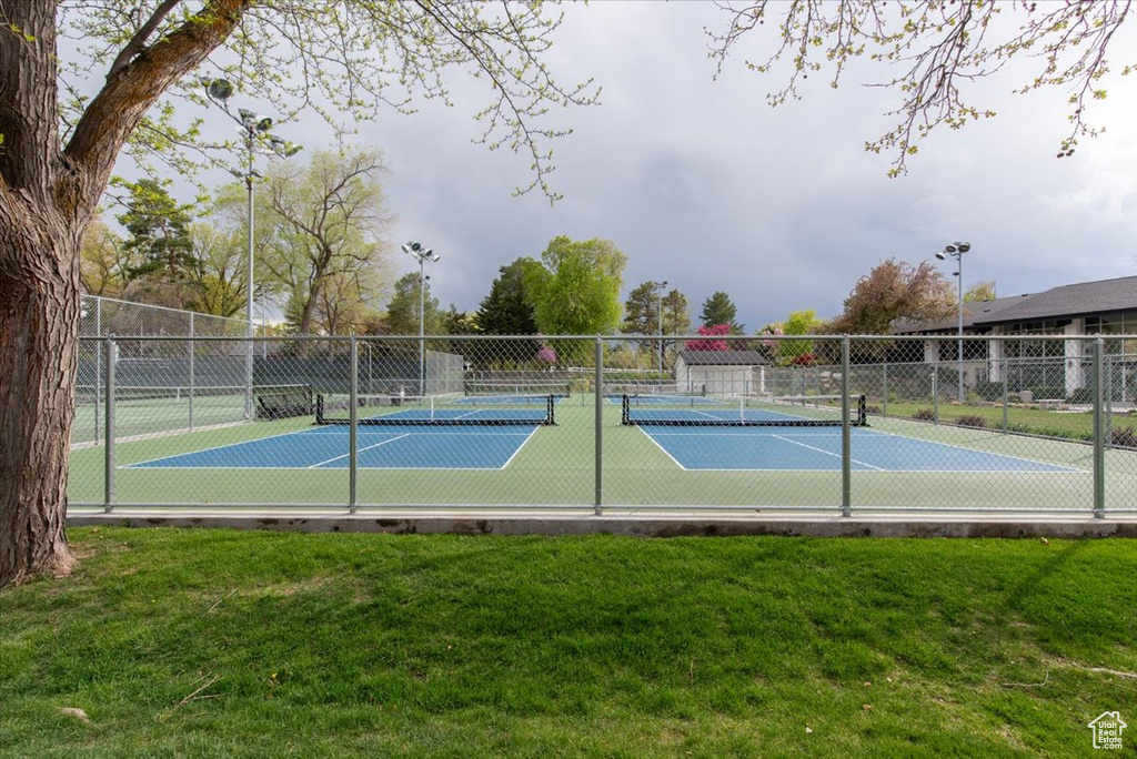 View of sport court featuring fence and a yard