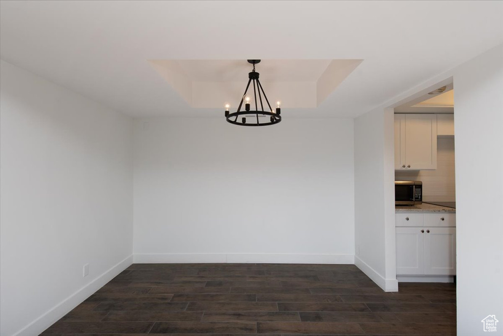Unfurnished dining area featuring baseboards, a notable chandelier, and dark wood-style floors