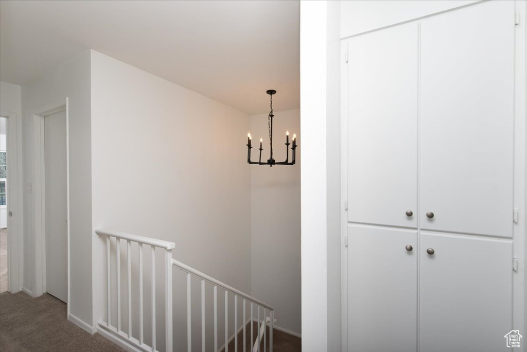 Hallway with baseboards, an inviting chandelier, an upstairs landing, and carpet