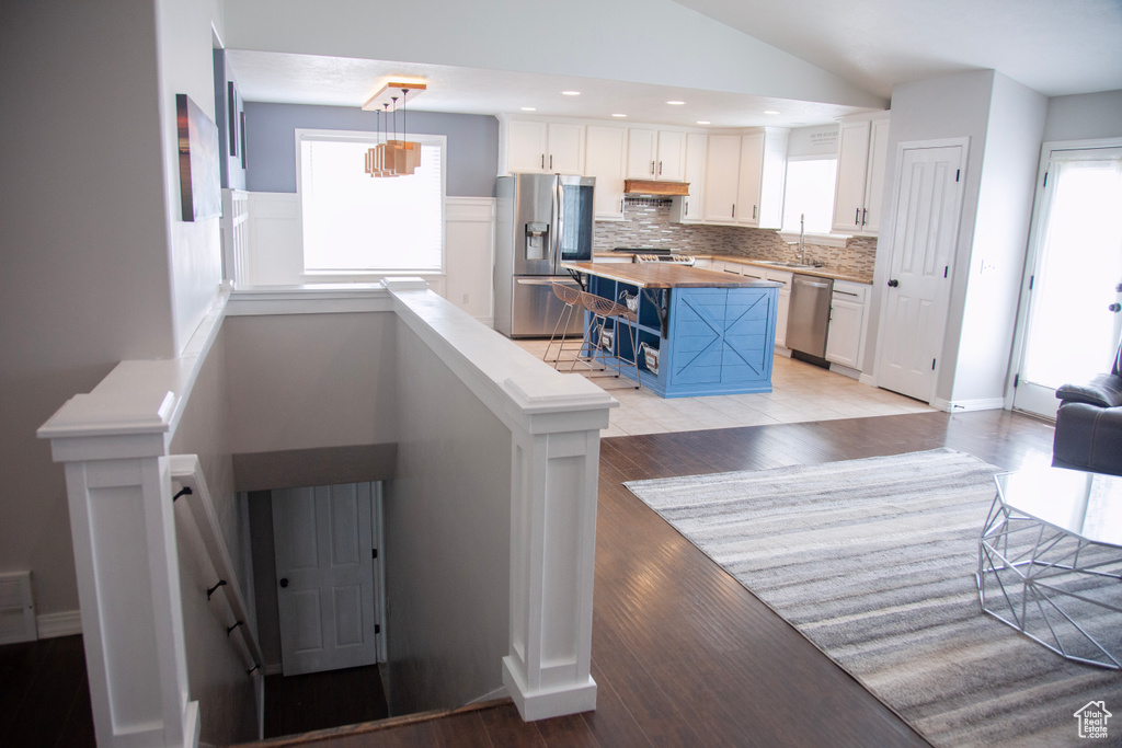 Interior space featuring white cabinets, appliances with stainless steel finishes, wooden counters, blue cabinets, and vaulted ceiling