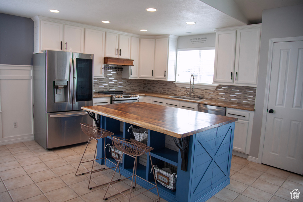 Kitchen with a sink, stainless steel appliances, open shelves, tasteful backsplash, and wooden counters