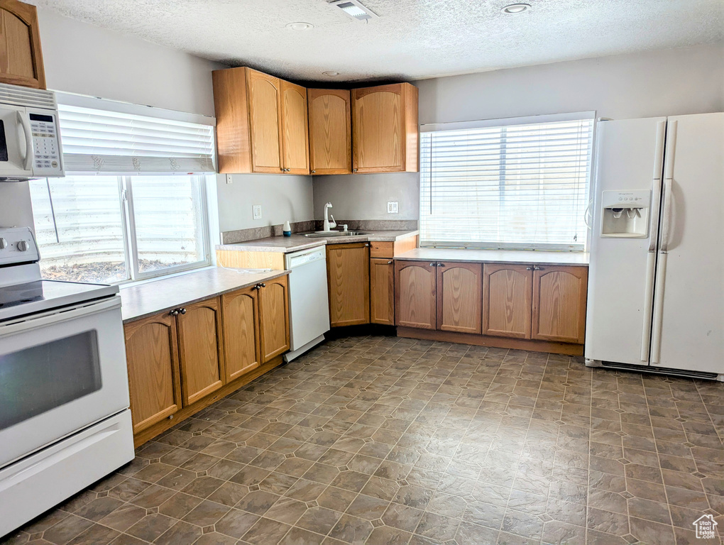 Kitchen with white appliances, a textured ceiling, healthy amount of natural light, a sink, and light countertops