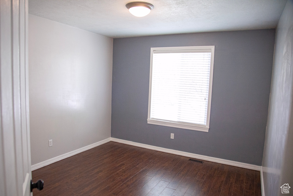 Spare room featuring dark wood-type flooring, visible vents, baseboards, and a healthy amount of sunlight