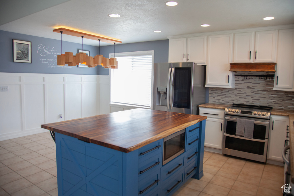 Kitchen with butcher block countertops, stainless steel appliances, blue cabinetry, a decorative wall, and premium range hood