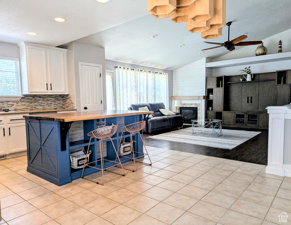 Kitchen featuring plenty of natural light, wooden counters, white cabinetry, light tile patterned floors, and lofted ceiling