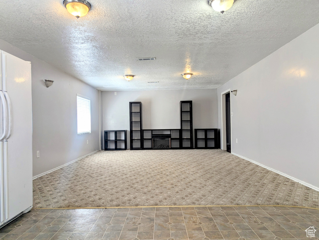Carpeted spare room with a textured ceiling and baseboards
