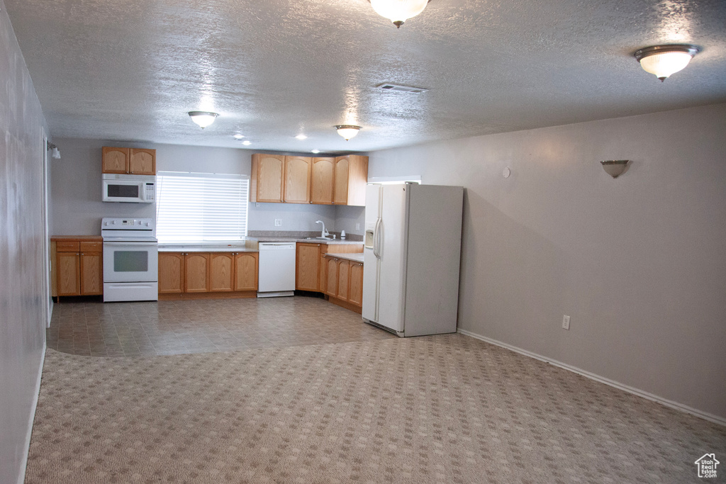 Kitchen featuring a textured ceiling, white appliances, light countertops, and baseboards