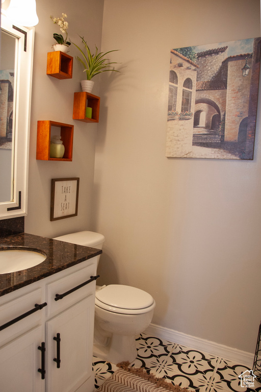 Half bath featuring toilet, tile patterned flooring, vanity, and baseboards