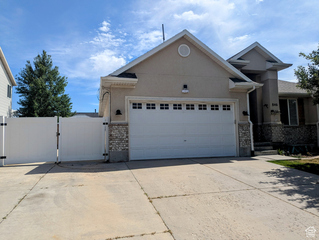 Ranch-style home with a gate, concrete driveway, an attached garage, stucco siding, and brick siding
