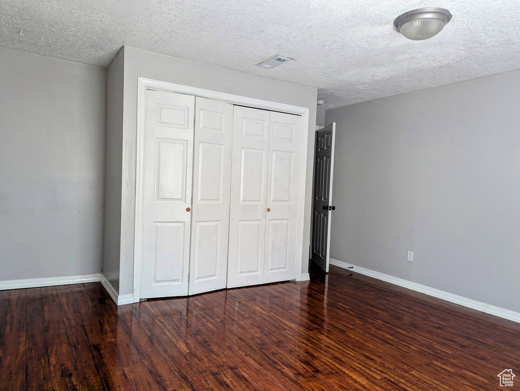 Unfurnished bedroom featuring a closet, wood finished floors, baseboards, and a textured ceiling