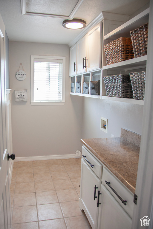Laundry room featuring washer hookup, light tile patterned floors, cabinet space, and baseboards