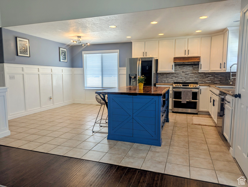 Kitchen featuring appliances with stainless steel finishes, under cabinet range hood, a center island, tasteful backsplash, and light tile patterned floors