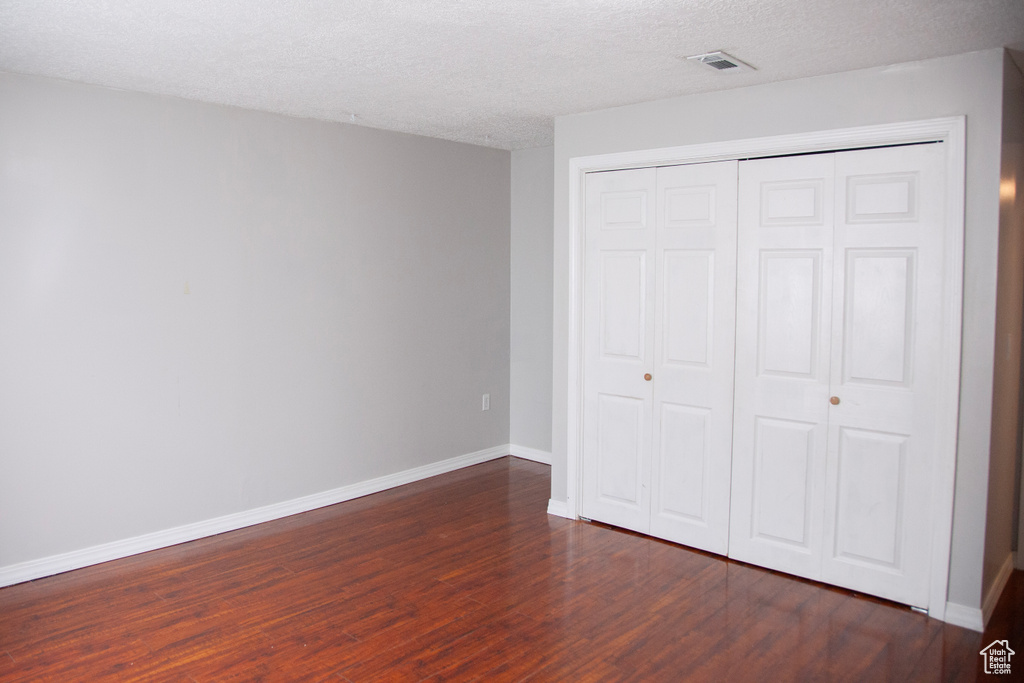 Unfurnished bedroom featuring dark wood-style floors, a closet, visible vents, baseboards, and a textured ceiling