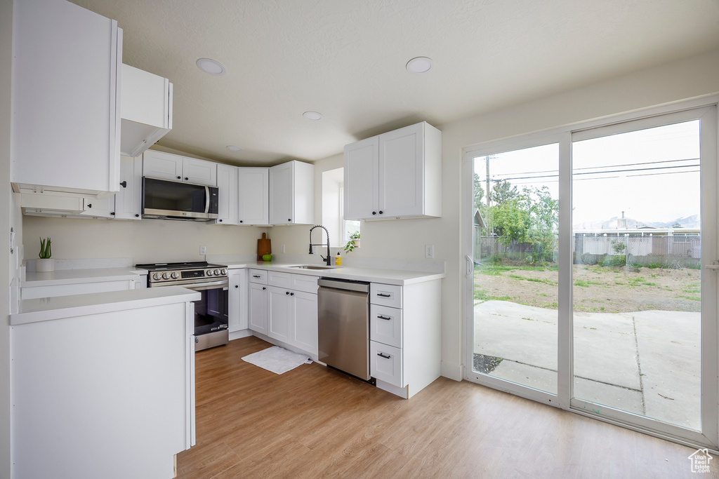 Kitchen featuring white cabinets, a sink, appliances with stainless steel finishes, light countertops, and light wood finished floors